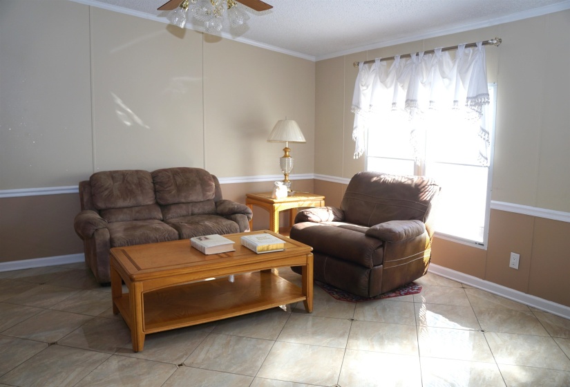 Living area featuring light tile patterned floors, baseboards, a ceiling fan, ornamental molding, and a textured ceiling