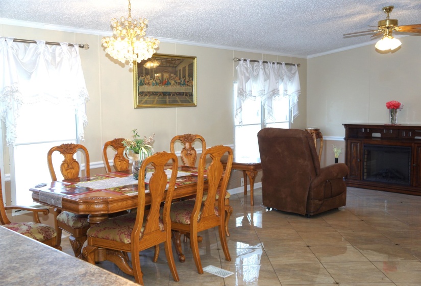 Dining area with a fireplace, crown molding, a textured ceiling, and ceiling fan with notable chandelier
