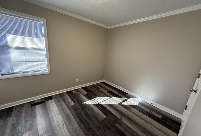 Empty room with visible vents, baseboards, dark wood-style floors, and ornamental molding