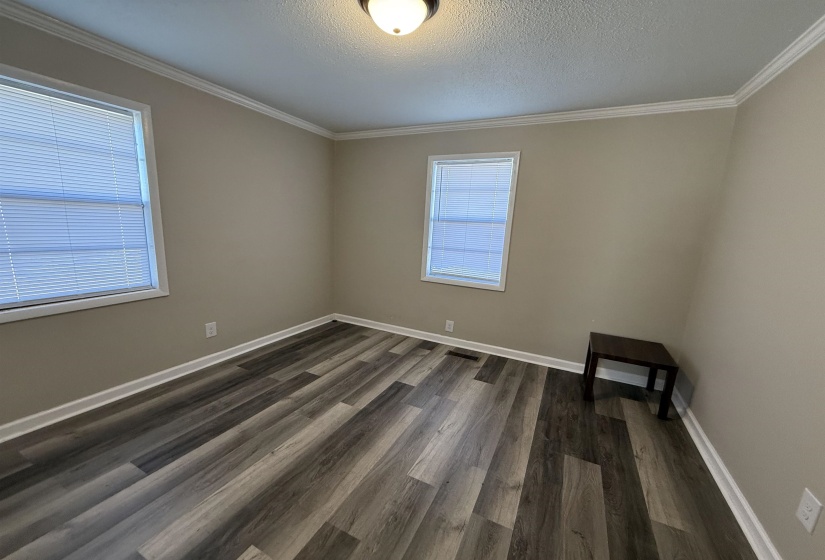 Empty room with crown molding, baseboards, dark wood-style flooring, and a textured ceiling