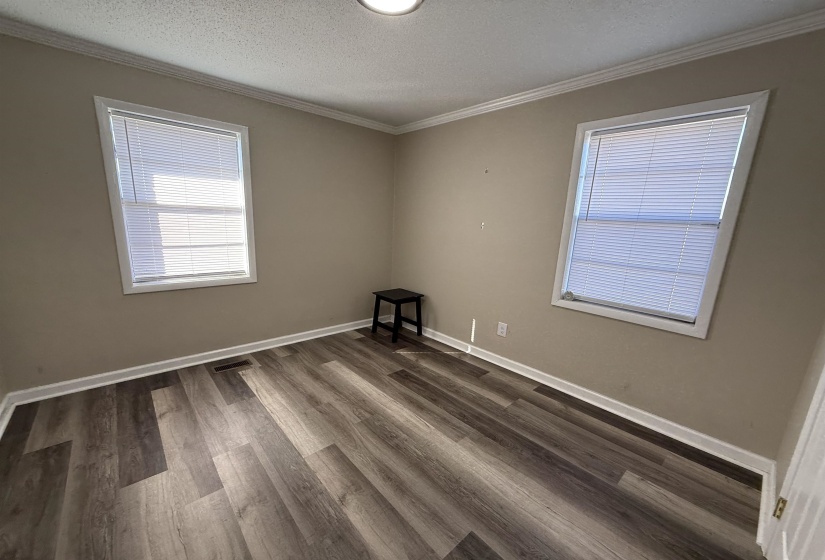 Empty room featuring crown molding, visible vents, dark wood-style flooring, and a textured ceiling