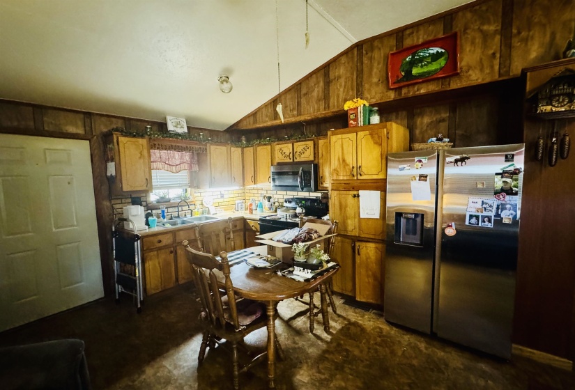 Kitchen with wood walls, lofted ceiling, appliances with stainless steel finishes, brown cabinetry, and a sink