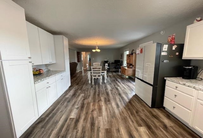 Kitchen featuring dark wood finished floors, white cabinets, freestanding refrigerator, and light stone countertops