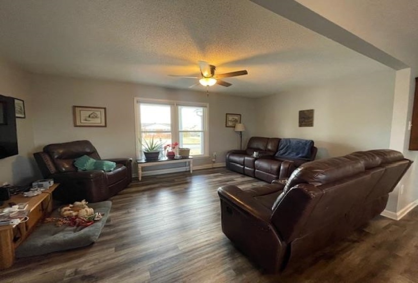 Living area featuring a textured ceiling, baseboards, dark wood-style flooring, and ceiling fan