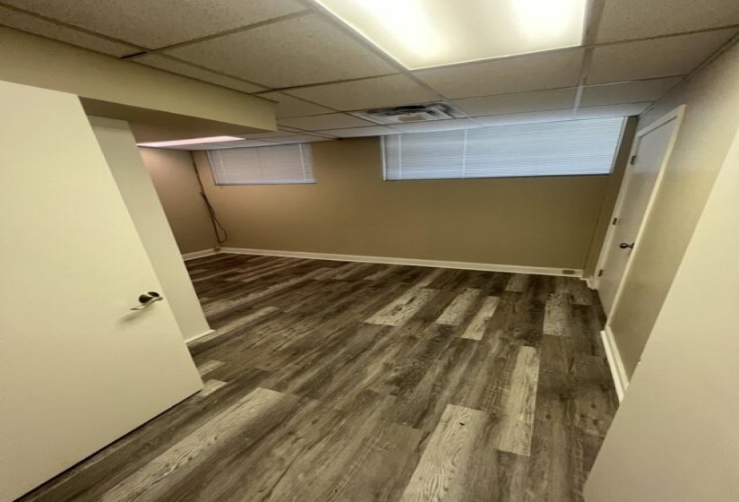 Finished below grade area with visible vents, a paneled ceiling, baseboards, and dark wood-style flooring