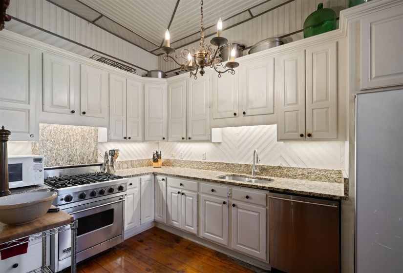 Kitchen with light stone counters, stainless steel appliances, white cabinetry, dark wood-type flooring, and sink