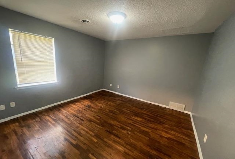Empty room with dark wood-type flooring, baseboards, a textured ceiling, and visible vents