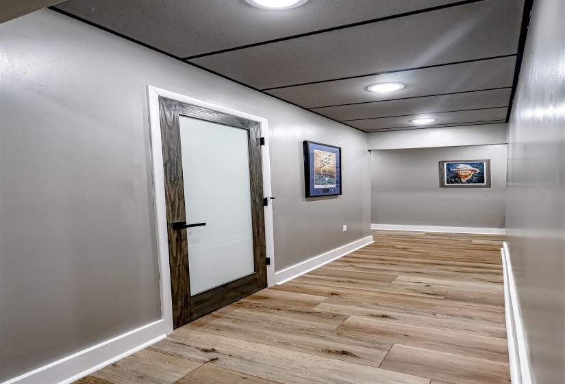 Hallway featuring baseboards, a paneled ceiling, and light wood-style floors