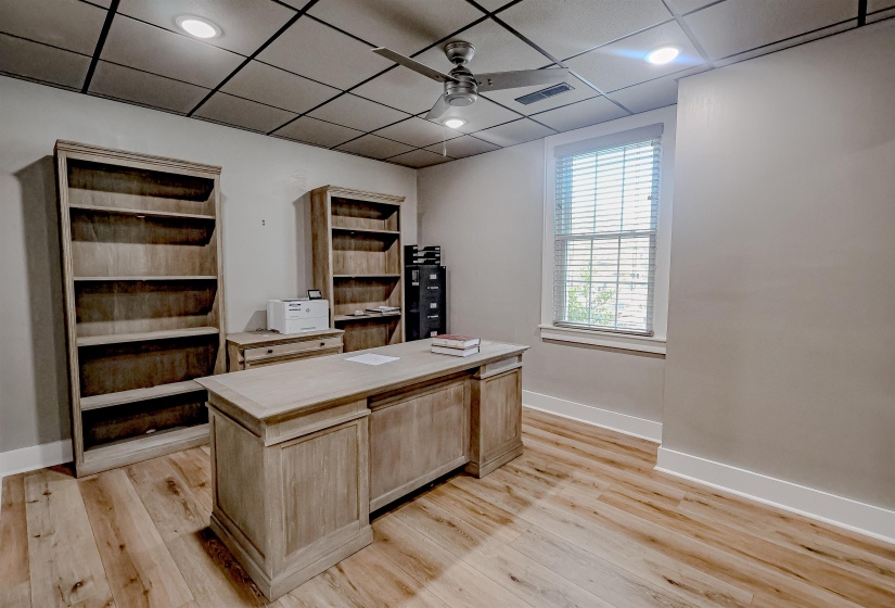 Office area featuring visible vents, baseboards, ceiling fan, a drop ceiling, and light wood-type flooring