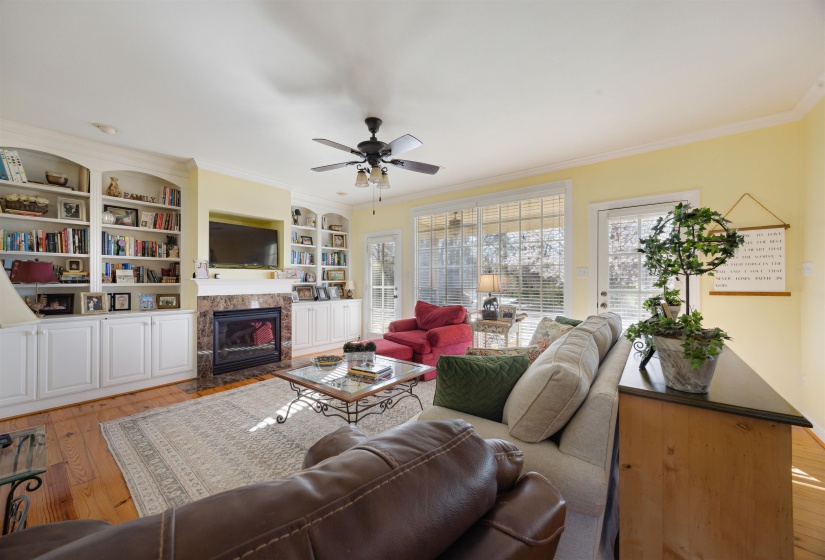 Living area featuring crown molding, light wood finished floors, a tiled fireplace, a ceiling fan, and built in features