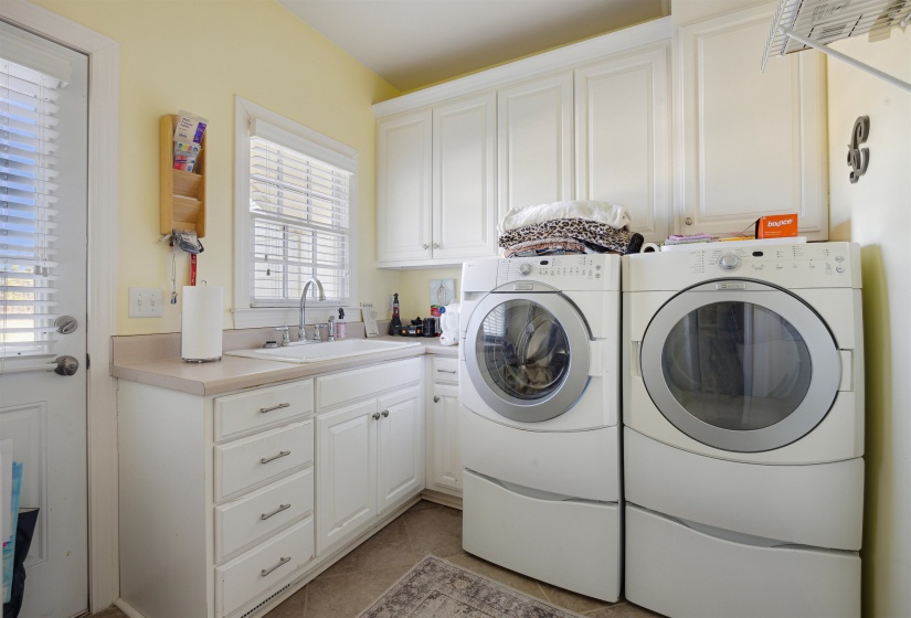 Clothes washing area with light tile patterned flooring, cabinet space, washing machine and dryer, and a sink