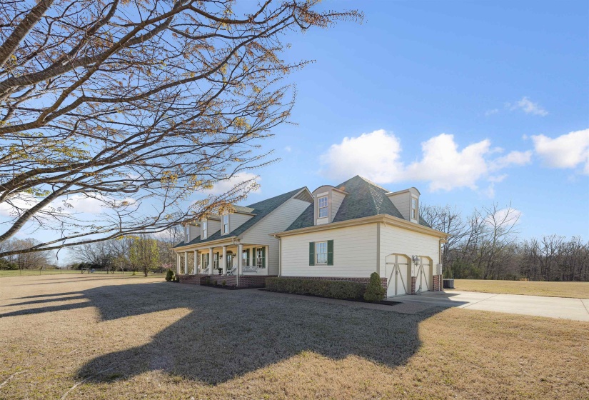 View of side of property featuring a yard, an attached garage, a porch, and concrete driveway
