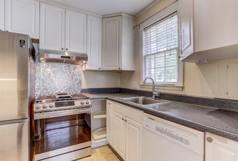 Kitchen with appliances with stainless steel finishes, dark countertops, white cabinets, under cabinet range hood, and decorative backsplash