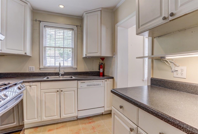 Kitchen featuring white dishwasher, gas range, dark countertops, white cabinets, and ornamental molding