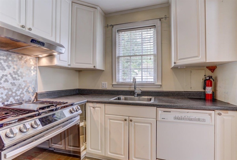 Kitchen featuring stainless steel range with gas stovetop, dishwasher, white cabinetry, dark countertops, and under cabinet range hood