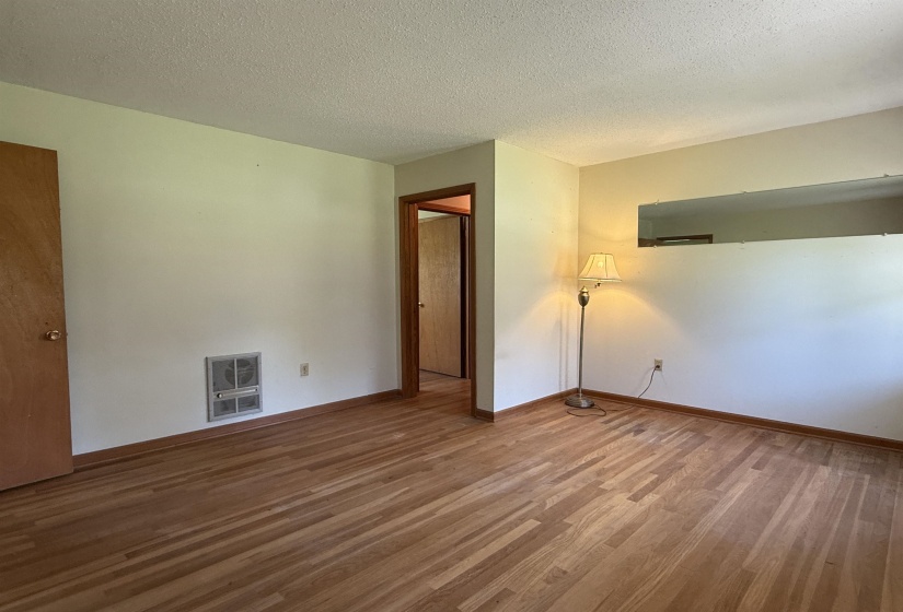 Empty room with a textured ceiling, baseboards, heating unit, and wood finished floors