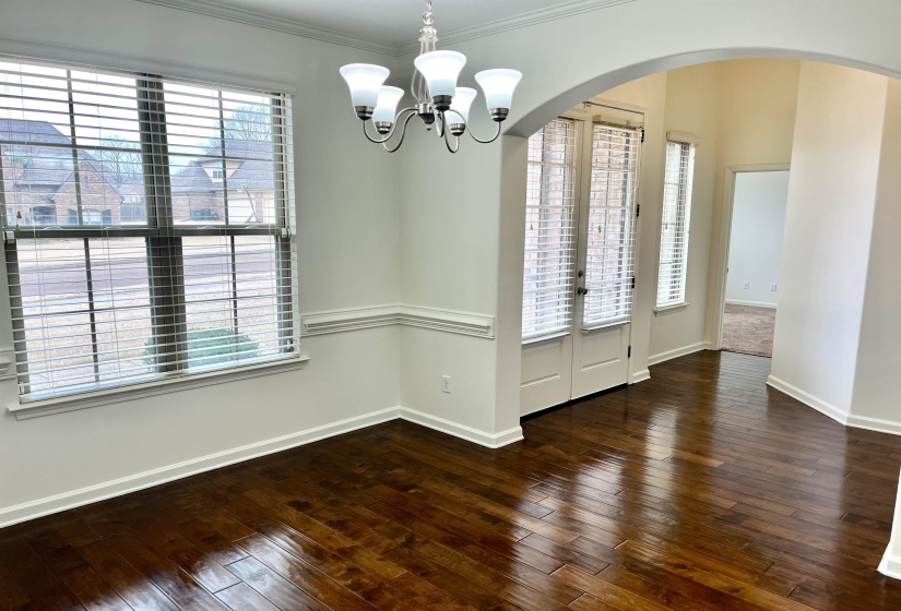 Interior space with crown molding, baseboards, arched walkways, a notable chandelier, and wood-type flooring