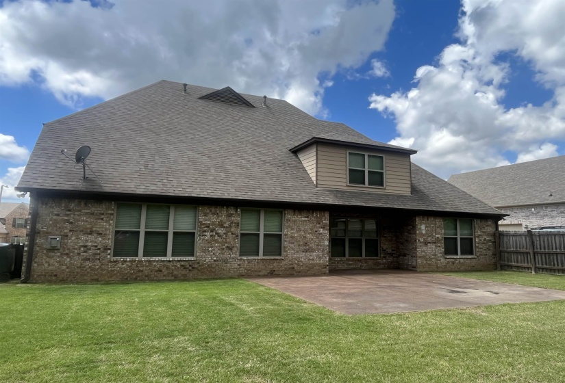 Back of property featuring roof with shingles, a patio area, brick siding, fence, and a yard