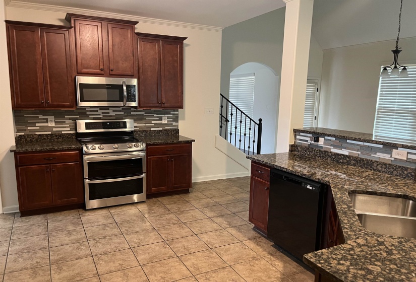 Kitchen with arched walkways, decorative backsplash, dark stone countertops, and stainless steel appliances