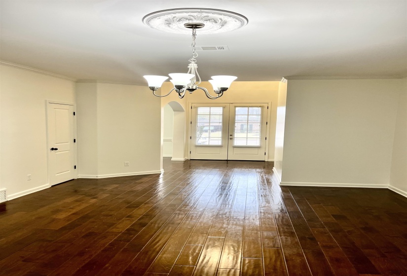Empty room with crown molding, a chandelier, dark wood-style floors, visible vents, and arched walkways