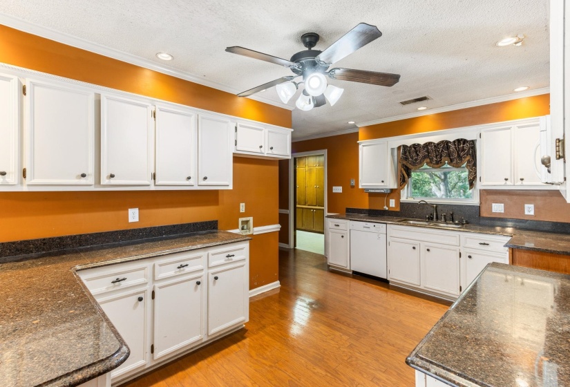 Kitchen featuring white cabinets, light wood finished floors, ornamental molding, white dishwasher, and dark stone countertops