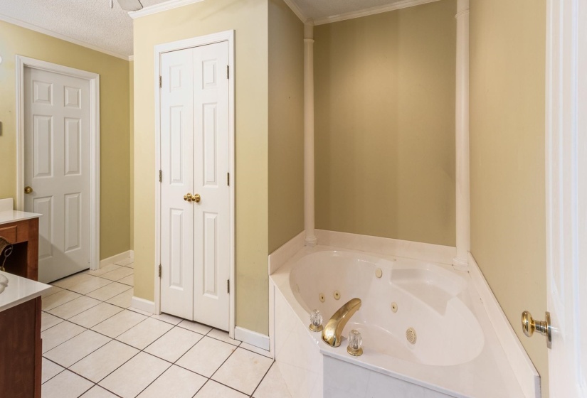 Full bathroom with a textured ceiling, vanity, light tile patterned flooring, a tub with jets, and crown molding