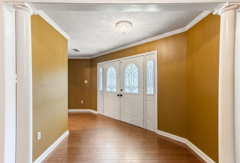 Entrance foyer with ornamental molding, ornate columns, a textured ceiling, and wood-type flooring