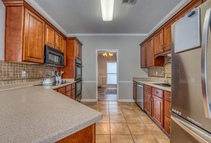 Kitchen featuring light tile patterned flooring, light countertops, crown molding, a sink, and black appliances
