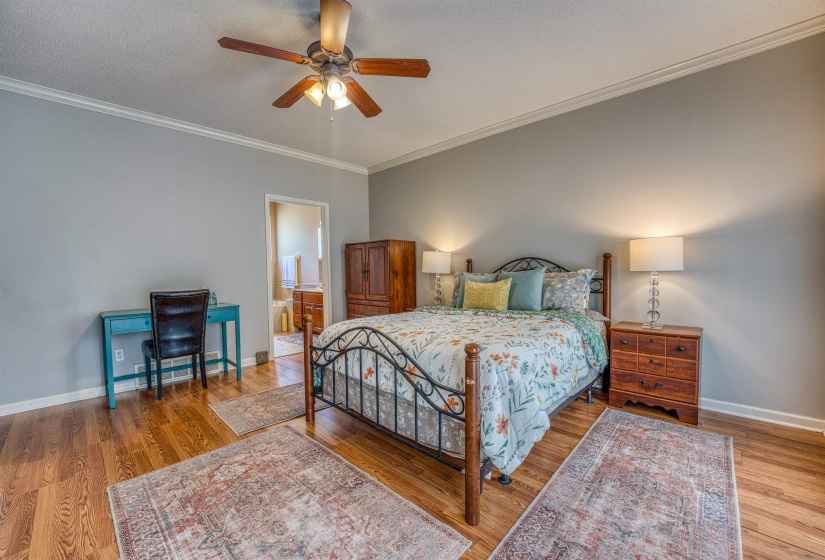 Bedroom featuring baseboards, a textured ceiling, ornamental molding, and wood finished floors
