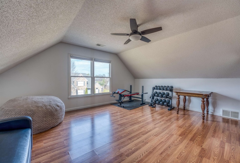 Workout room with ceiling fan, visible vents, wood finished floors, and lofted ceiling