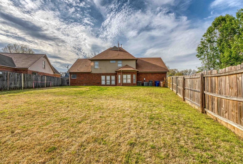 Back of property with a lawn, brick siding, central air condition unit, and a fenced backyard