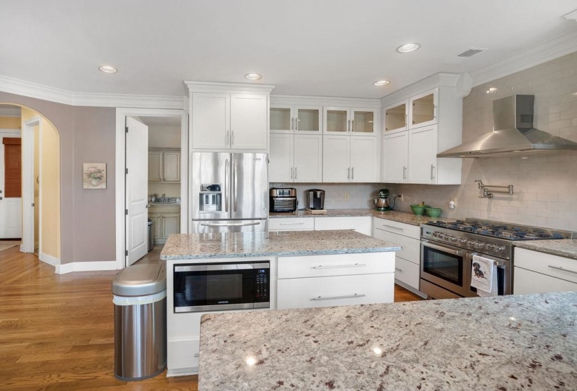 Kitchen featuring crown molding, light wood finished floors, stainless steel appliances, arched walkways, and wall chimney range hood