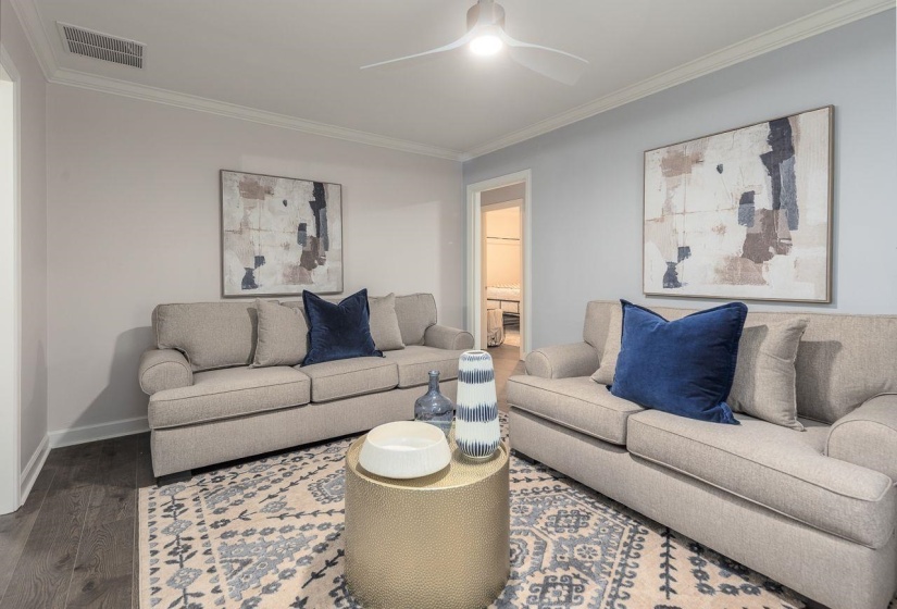 Living area with dark wood-style floors, visible vents, a ceiling fan, and ornamental molding