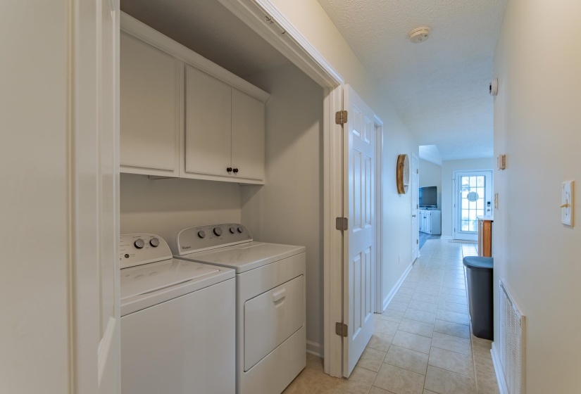 Clothes washing area featuring light tile patterned floors, baseboards, washing machine and clothes dryer, visible vents, and cabinet space