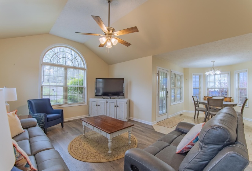 Living area featuring ceiling fan with notable chandelier, baseboards, vaulted ceiling, and wood finished floors