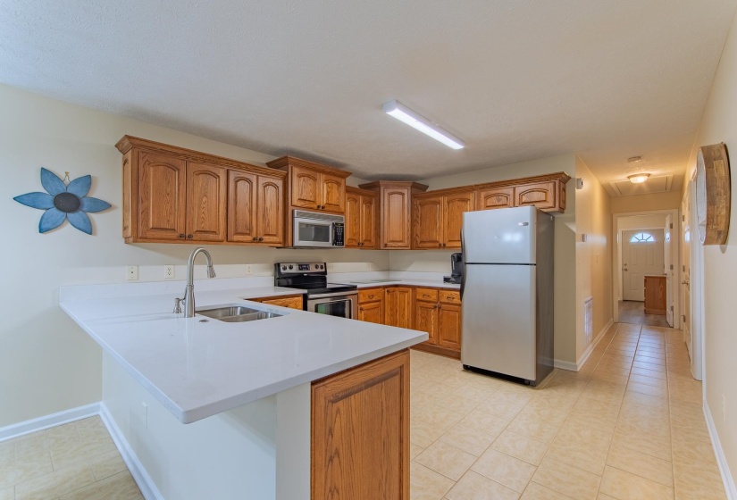 Kitchen with light countertops, a sink, a peninsula, brown cabinetry, and stainless steel appliances