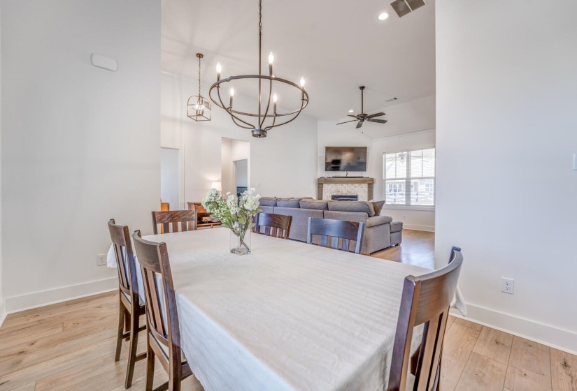 Dining area featuring a fireplace, light wood-type flooring, baseboards, ceiling fan with notable chandelier, and visible vents