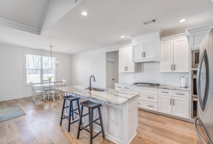 Kitchen with a sink, light stone countertops, light wood-style flooring, visible vents, and decorative backsplash