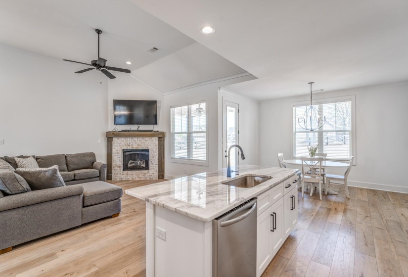 Kitchen featuring light stone counters, a sink, a fireplace, stainless steel dishwasher, and white cabinets