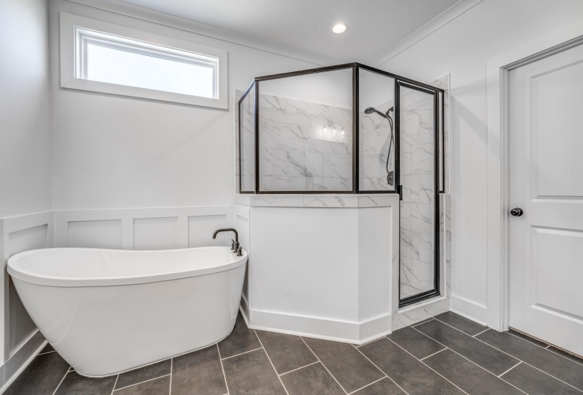 Bathroom featuring a freestanding bath, a decorative wall, wainscoting, and a marble finish shower