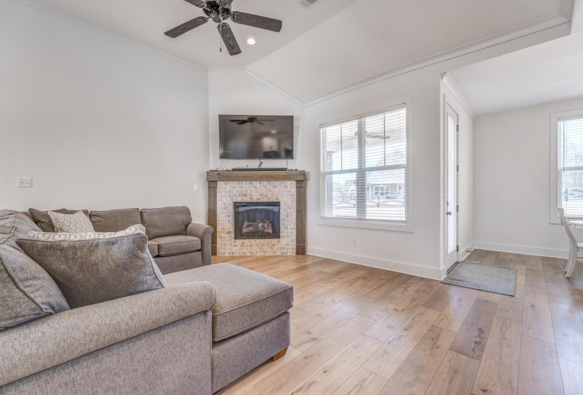 Living room featuring a ceiling fan, a brick fireplace, light wood-style flooring, baseboards, and ornamental molding