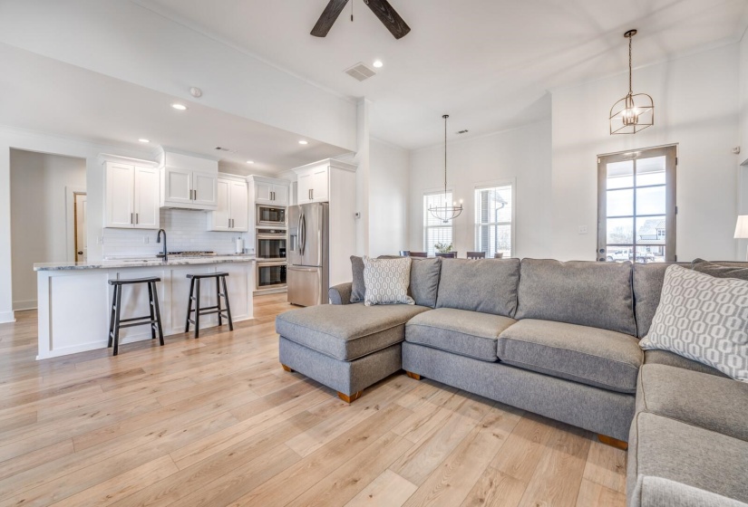 Living area featuring light wood-type flooring, recessed lighting, ceiling fan with notable chandelier, baseboards, and visible vents