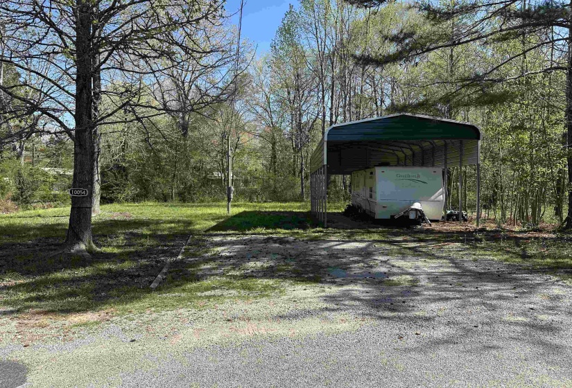 Exterior space featuring a detached carport, a forest view, and dirt driveway