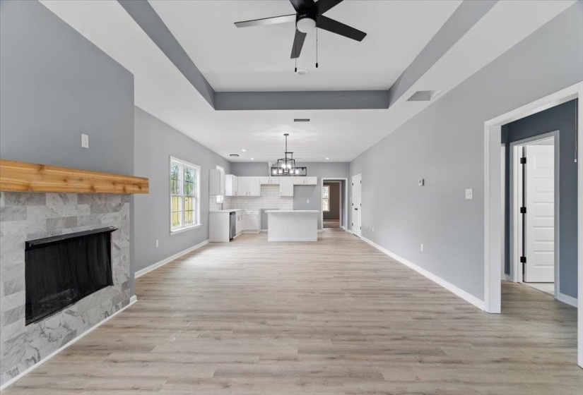 Unfurnished living room featuring light wood-type flooring, ceiling fan with notable chandelier, baseboards, and visible vents