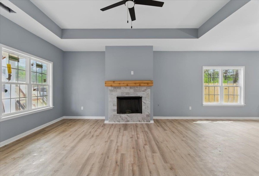 Unfurnished living room featuring baseboards, a tray ceiling, wood finished floors, and ceiling fan