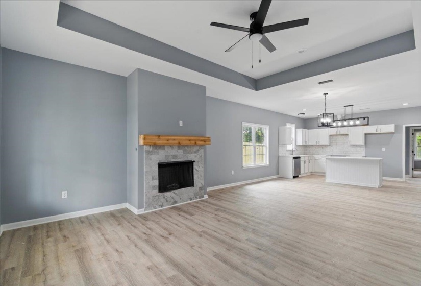 Unfurnished living room with a tray ceiling, light wood finished floors, a fireplace, ceiling fan with notable chandelier, and baseboards