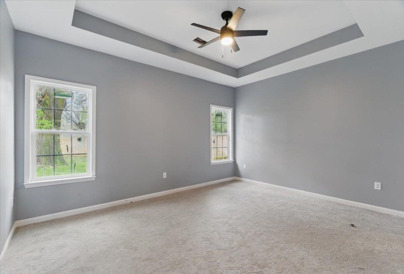 Spare room with baseboards, carpet flooring, a tray ceiling, and ceiling fan