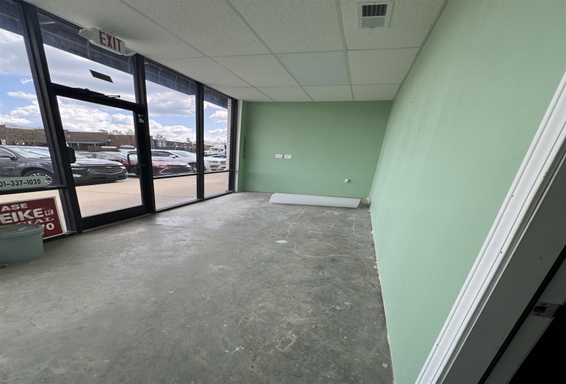 Unfurnished room featuring a wall of windows, concrete flooring, a drop ceiling, and visible vents