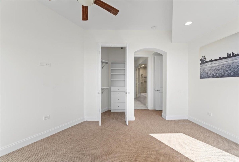 Unfurnished bedroom with arched walkways, light colored carpet, baseboards, and a spacious closet
