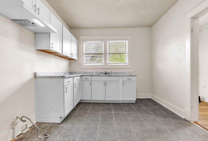 Kitchen featuring a sink, white cabinets, a textured ceiling, and under cabinet range hood